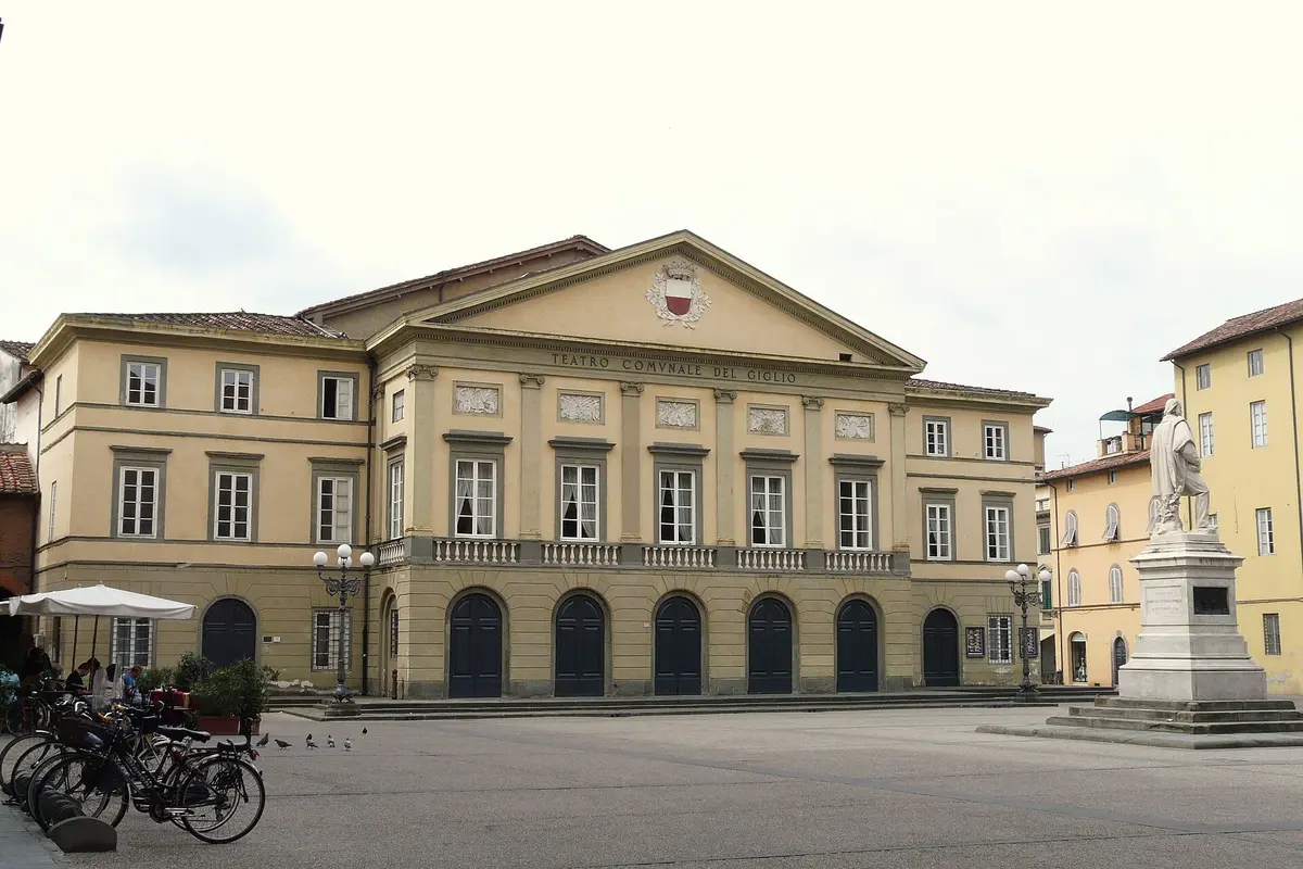 Den lysegule nyklassicistiske facade på Teatro del Giglio i Lucca, med en række bueformede døråbninger i gadeplan og en trekantet fronton ovenover, set på tværs af en åben plads